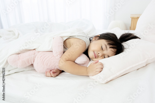 Portrait of a little girl sleeping in bed with a pink teddy bear at home