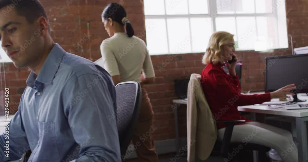 Diverse group of business colleagues sitting at desks, reading document talking on smartphone Diverse group of business colleagues sitting at desks, reading document talking on smartphone