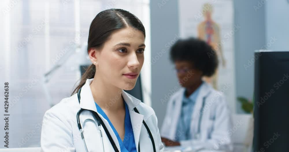 Close up portrait of Caucasian concentrated young woman doctor looking at monitor while typing on computer working in clinic. Female healthcare worker in white medical coat work in hospital Close up portrait of Caucasian concentrated young woman doctor looking at monitor while typing on computer working in clinic. Female healthcare worker in white medical coat work in hospital
