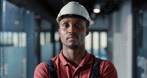 African young engineer worker electricity specialist wearing hardhat and uniform using tablet computer for managing lighting electric system inside office.
