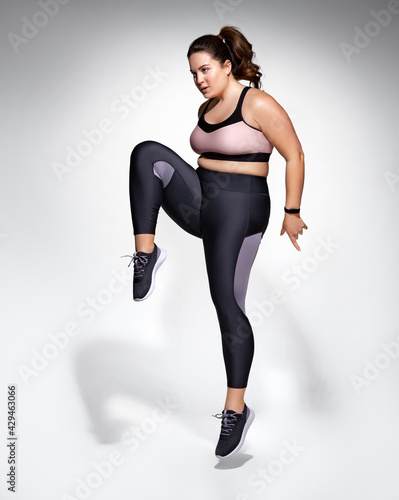 Warming up before training. Photo of model with curvy figure in fashionable sportswear on grey background. Sports motivation and healthy lifestyle