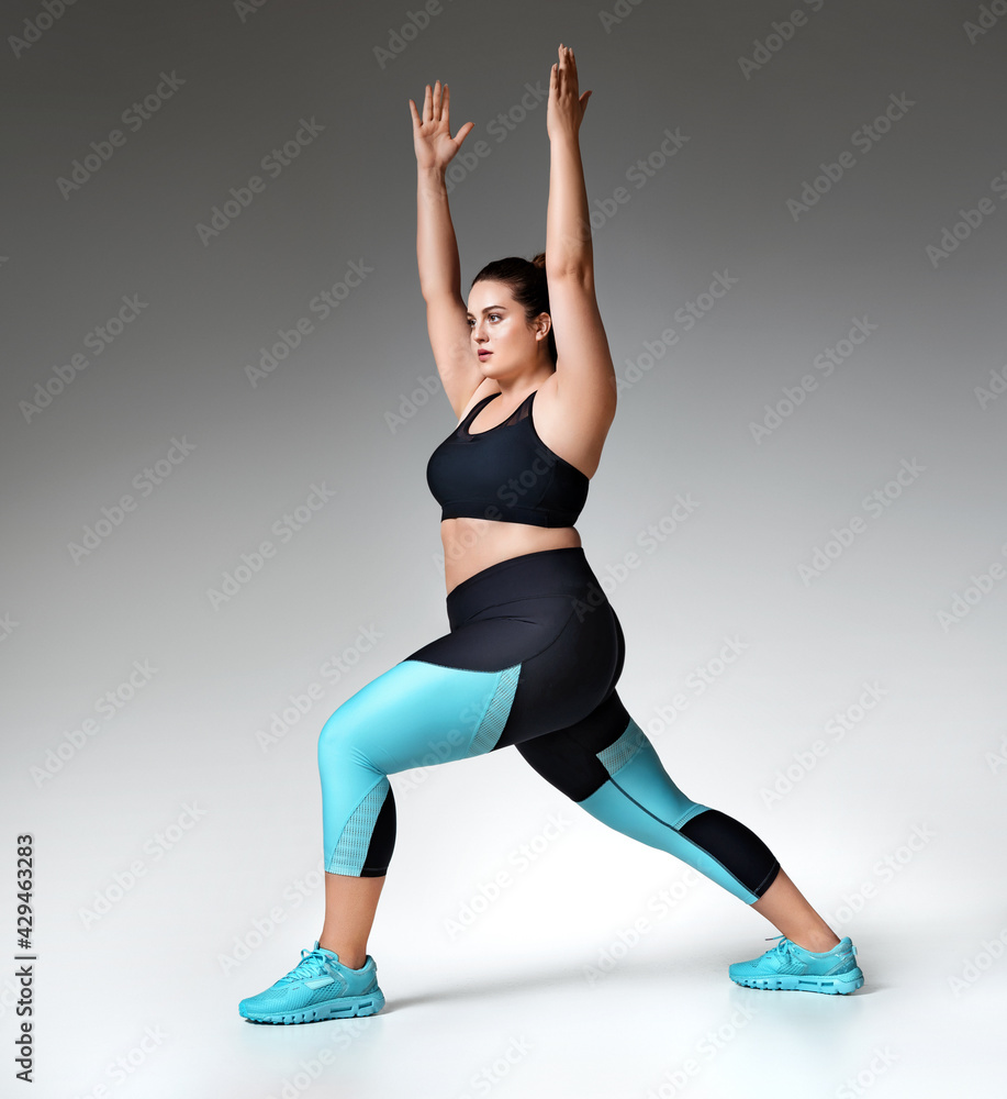 Warming up before training. Photo of model with curvy figure in fashionable sportswear on grey background. Sports motivation and healthy lifestyle Warming up before training. Photo of model with curvy figure in fashionable sportswear on grey background. Sports motivation and healthy lifestyle