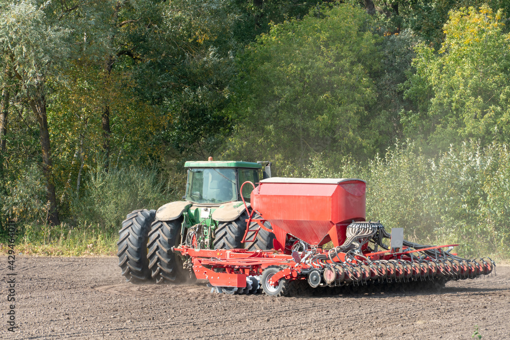 Fototapeta premium Sowing equipment works on the field on a dry summer day. Season to sow cereals. A farmer driving a tractor with a cultivator.