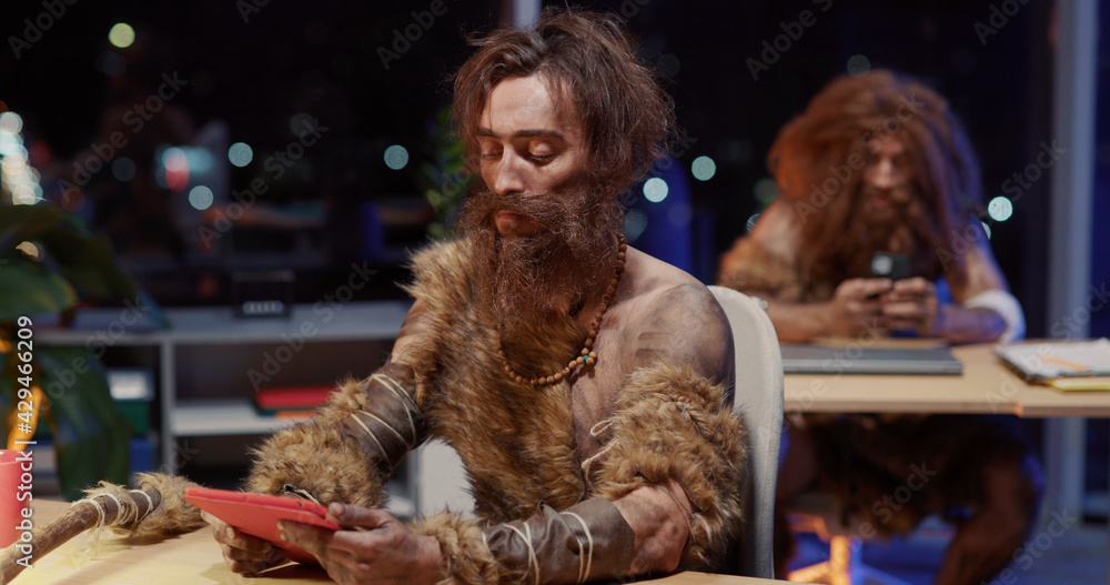 Portrait of Successful Prehistoric Savage in Animal Fur Using Tablet Earning Money Interacting Technology Learning Computer Clenching Fist to Camera.