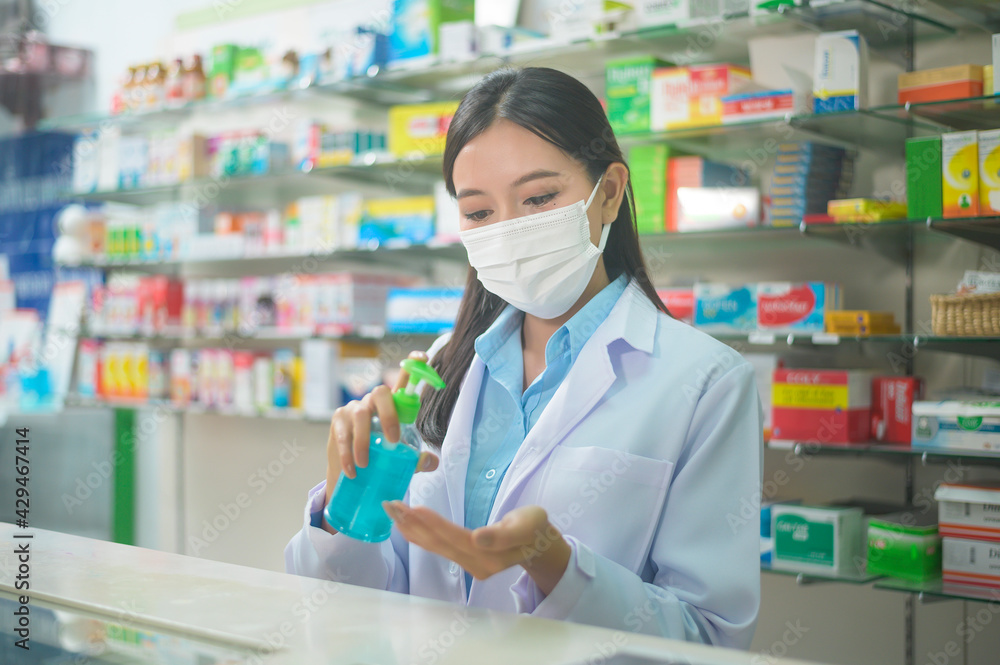 Portrait of asian woman pharmacist wearing a surgical mask using alcohol gel in a modern pharmacy drugstore, covid-19 and pandemic concept.