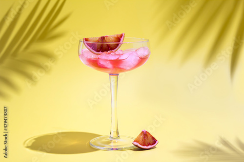 Party pink juice cocktail and ice with red oranges in glass on yellow background. Summer drinks