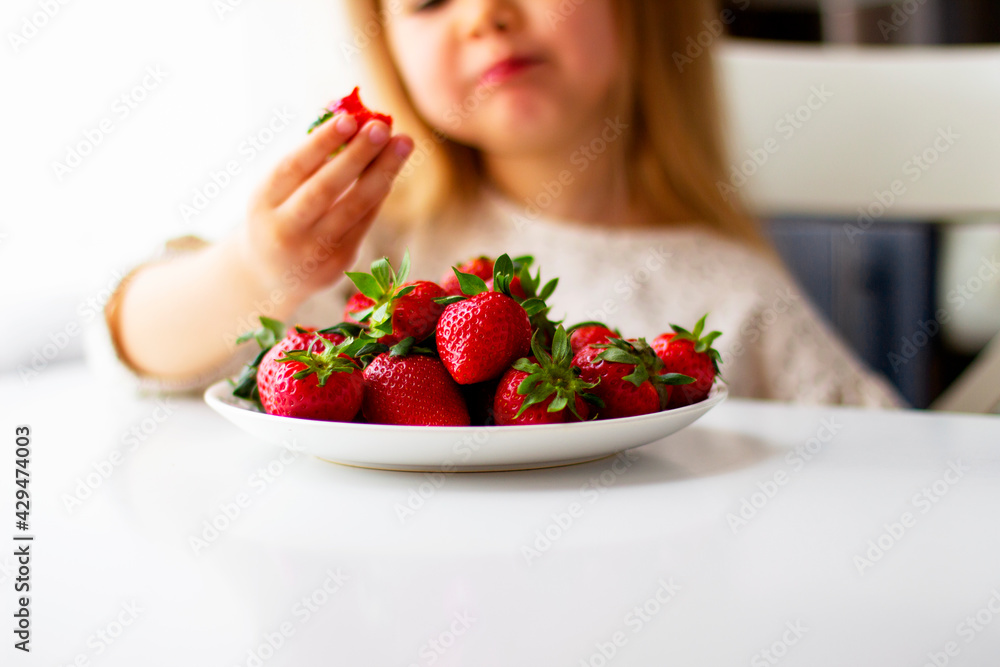 Cute little girl eating fresh strawberry in the kitchen. Healthy vitamin snack for kids. Ripe fresh berries. Harvest season. Natural vitamins . Cute little girl eating fresh strawberry in the kitchen. Healthy vitamin snack for kids. Ripe fresh berries. Harvest season. Natural vitamins .