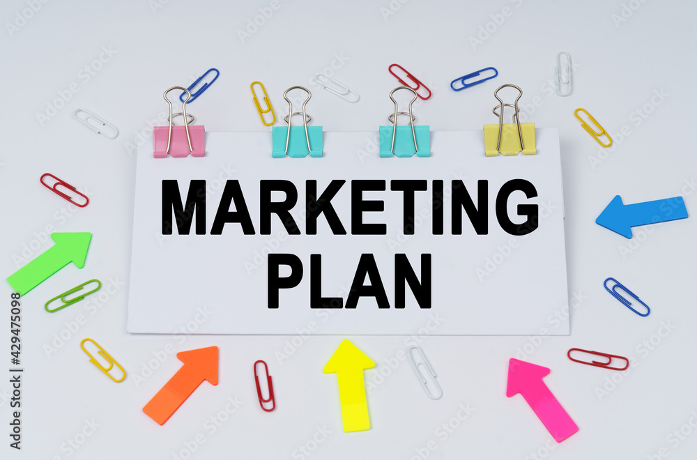 On the table there are paper clips and directional arrows, a sign that says - Marketing Plan On the table there are paper clips and directional arrows, a sign that says - Marketing Plan
