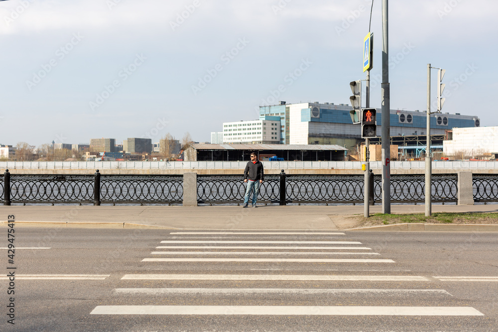 A man stands at a pedestrian crossing across the road