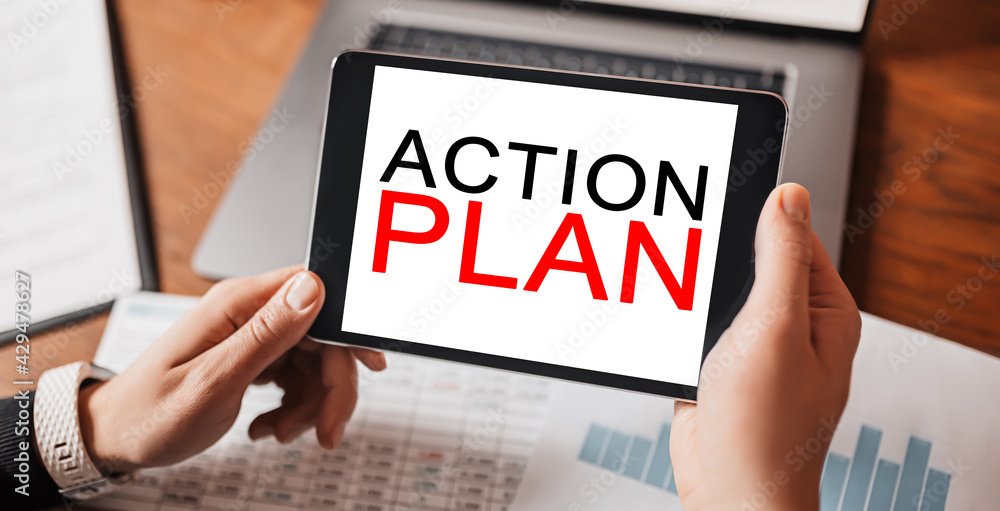 Man hands holding tablet with text ACTION PLAN at workplace. Businessman working at desk with documents Man hands holding tablet with text ACTION PLAN at workplace. Businessman working at desk with documents