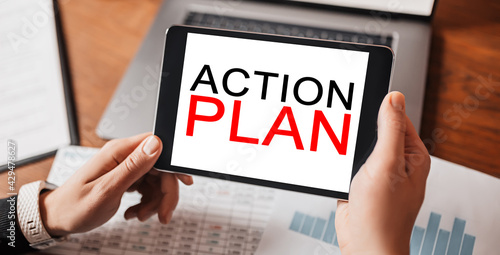 Man hands holding tablet with text ACTION PLAN at workplace. Businessman working at desk with documents