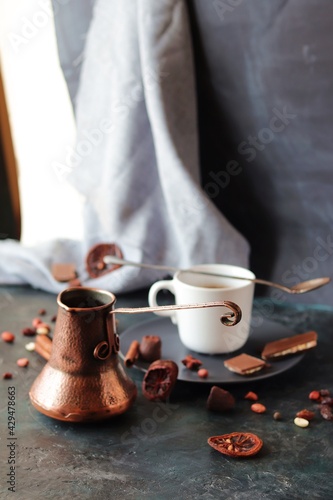 Cup with hot coffee, copper coffee maker, chocolate and spices on the table, dark background, home kitchen
