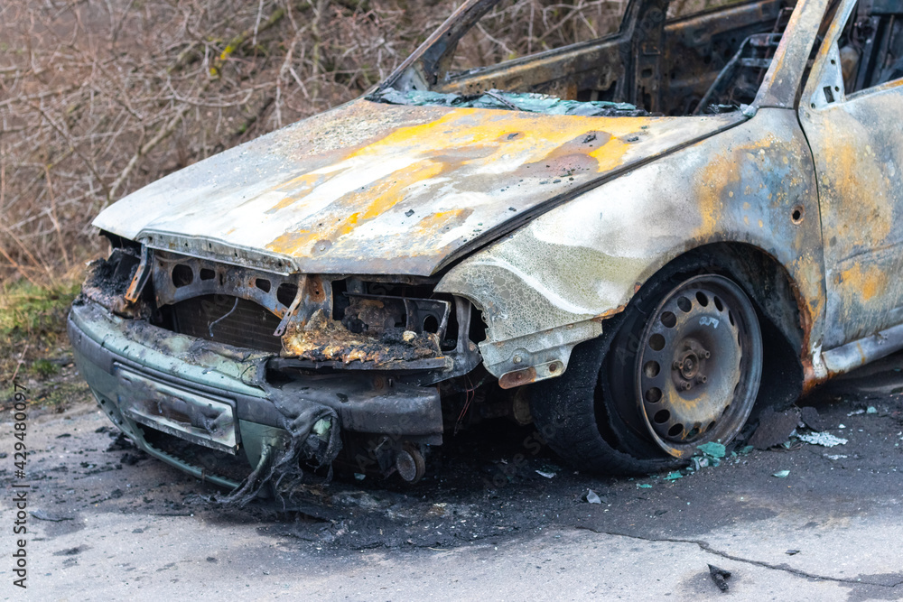 Burned car after an accident on the asphalt road. Close-up, fragment. Arson of a car, criminal showdowns Burned car after an accident on the asphalt road. Close-up, fragment. Arson of a car, criminal showdowns