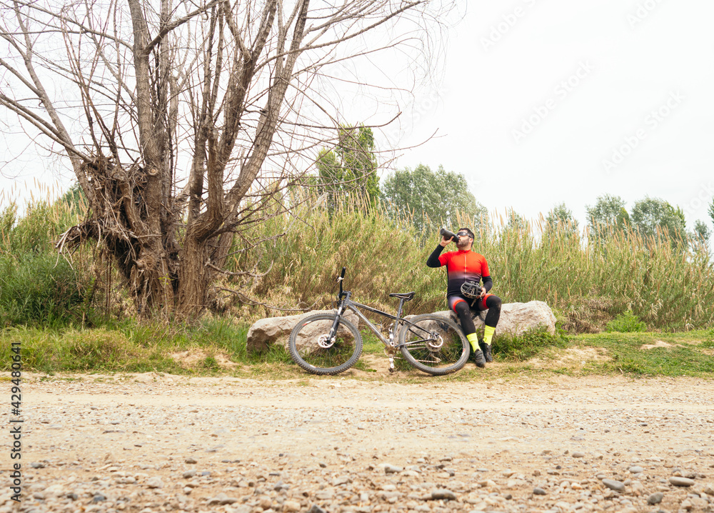 Obraz premium Male cyclist drinks water next to his mountain bike in nature