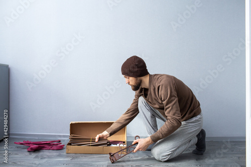 bearded man unpacks a box of furniture parts.