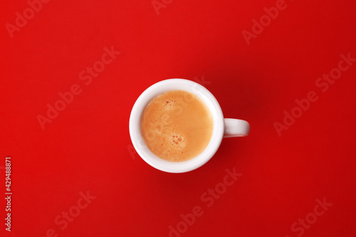 white cup of coffee with foam on a red background top view 