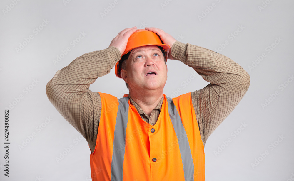 contruction worker clutching his head in helmet on grey studio background looking up, foreman shocked contruction worker clutching his head in helmet on grey studio background looking up, foreman shocked