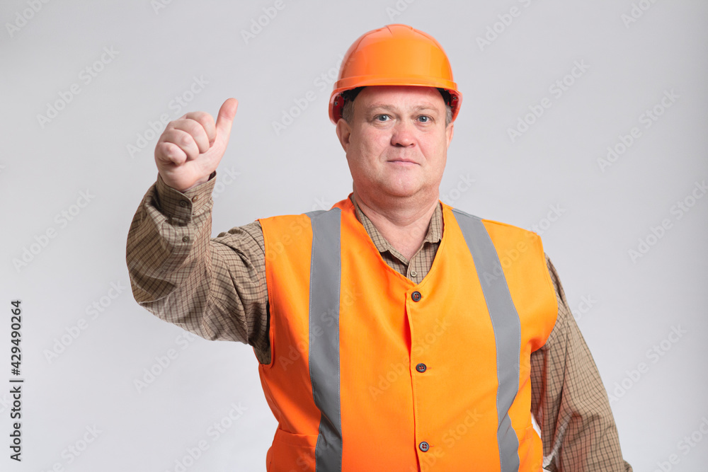 successful construction worker in hard hat showing thumb up on grey background good-natured fat engineer