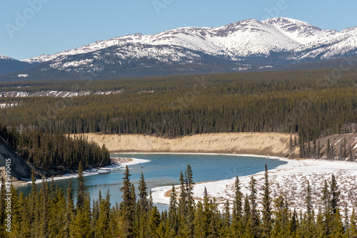 Winding Yukon River outside of Whitehorse in spring time with wonderful scenic view of the wilderness surrounding snow capped mountain peaks in the background. Desktop wallpaper, tourism, visit.  © Scalia Media