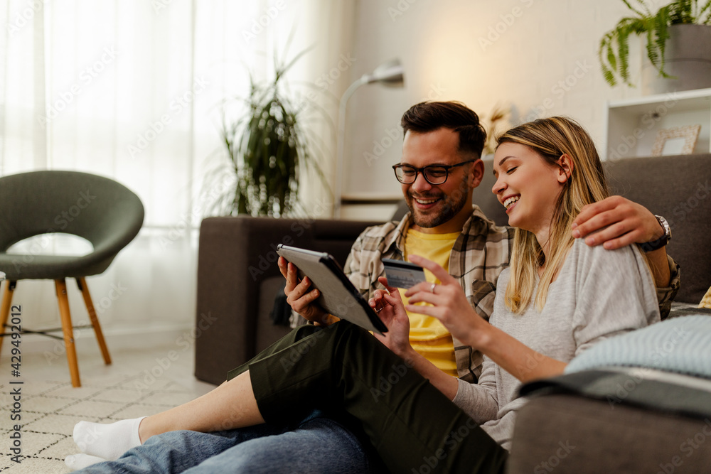 Cute Caucasian sitting on the floor and using tablet for online shopping. Woman holding credit card. Cute Caucasian sitting on the floor and using tablet for online shopping. Woman holding credit card.