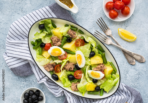 American version of Nicoise salad with canned tuna, boiled potatoes and green asparagus beans in an oval white dish on a gray concrete plate.