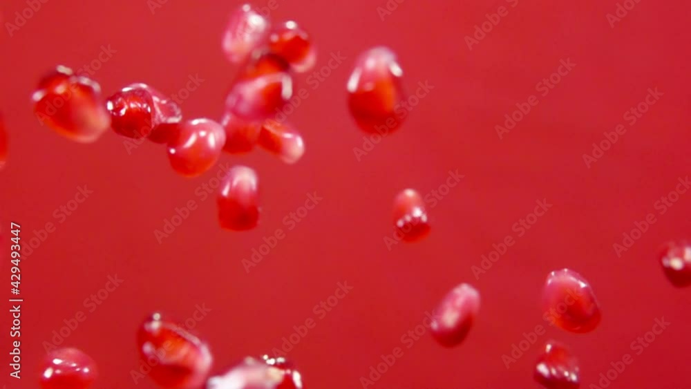 Juicy ripe pomegranate grains are flying up and falling down on the red background in slow motion Juicy ripe pomegranate grains are flying up and falling down on the red background in slow motion