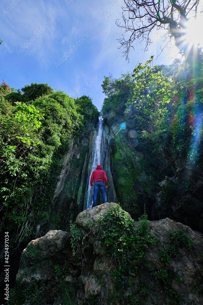 Young man with a red hood looking at the Chorrera de Balastar Waterfalls, Faraján. Unique corner of the province of Malaga in Andalusia