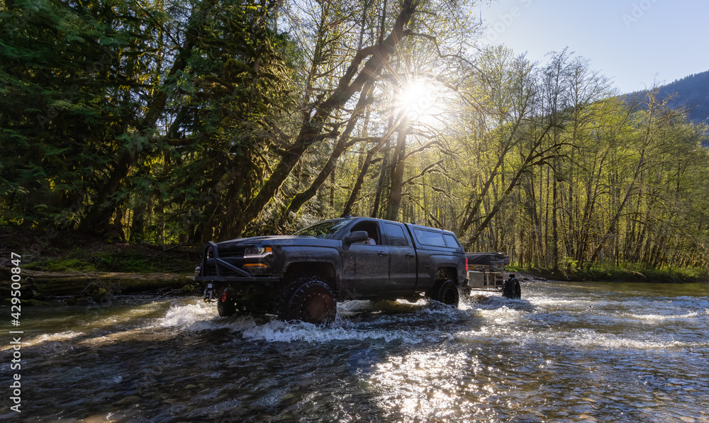 Custom 4x4 Truck with raised suspension wheels riding across a river in the rain forest during a sunny spring day. Located in Squamish Valley, North of Vancouver, British Columbia, Canada. Custom 4x4 Truck with raised suspension wheels riding across a river in the rain forest during a sunny spring day. Located in Squamish Valley, North of Vancouver, British Columbia, Canada.