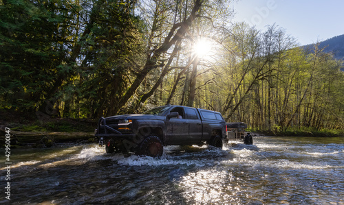 Custom 4x4 Truck with raised suspension wheels riding across a river in the rain forest during a sunny spring day. Located in Squamish Valley, North of Vancouver, British Columbia, Canada.