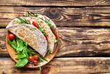 Piadina Romagnola with mozzarella cheese, tomatoes, ham and rocket salad on wooden table. Italian flatbread or open sandwich. Selective focus. Top view.