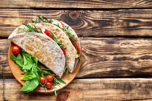 Piadina Romagnola with mozzarella cheese, tomatoes, ham and rocket salad on wooden table. Italian flatbread or open sandwich. Selective focus. Top view. photo