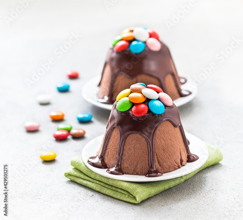 Chocolate dessert cottage cheese Easter, poured with icing and decorated with colorful candies on a plate on a linen napkin on a light gray background