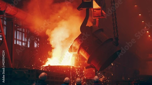 Pouring bright hot liquid steel or metal from ladle in blast furnace foundry metallurgical factory. Steel mill iron smelting process with bright sparks and smoke.