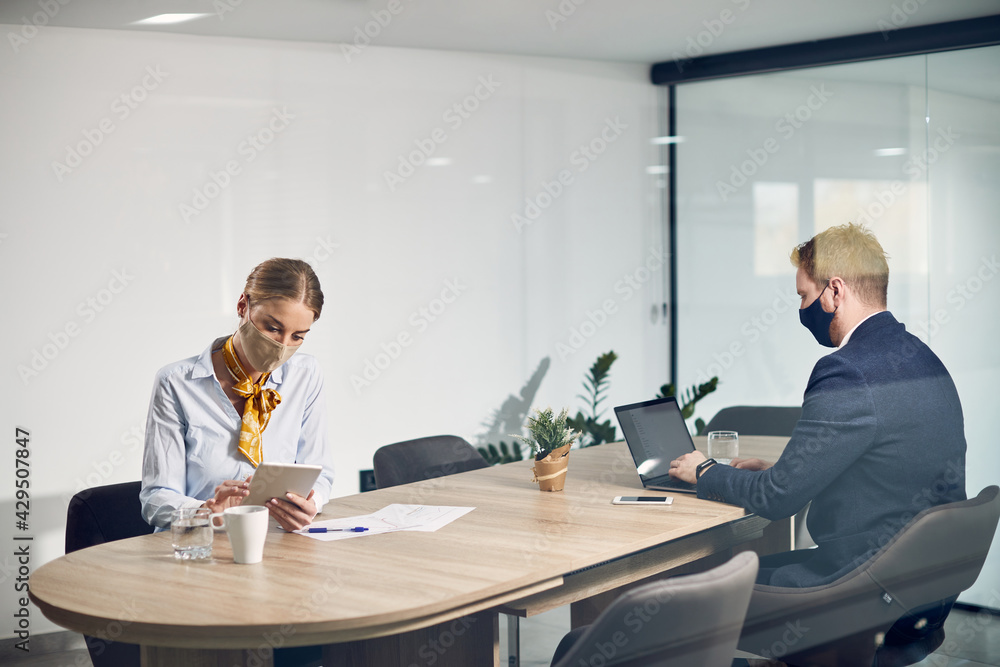 Business colleagues with face masks working on wireless technology while sitting apart from each other due to coronavirus pandemic. Business colleagues with face masks working on wireless technology while sitting apart from each other due to coronavirus pandemic.
