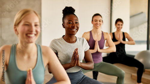 Happy African American female athlete practicing Yoga with group of women at health club.