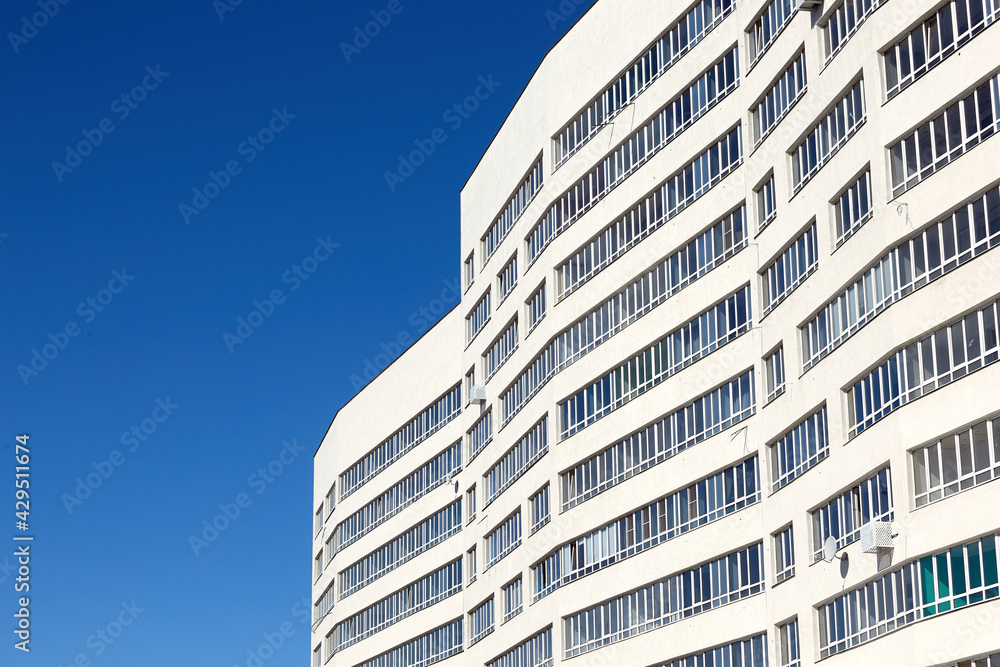 A fragment of modern architecture, walls and glass. Windows and balconies of a residential building against a blue sky A fragment of modern architecture, walls and glass. Windows and balconies of a residential building against a blue sky