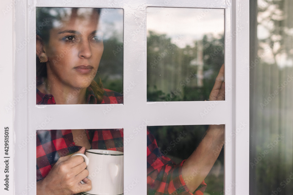 outside view of a Latina woman during isolation looking out the window. Selective focus outside view of a Latina woman during isolation looking out the window. Selective focus