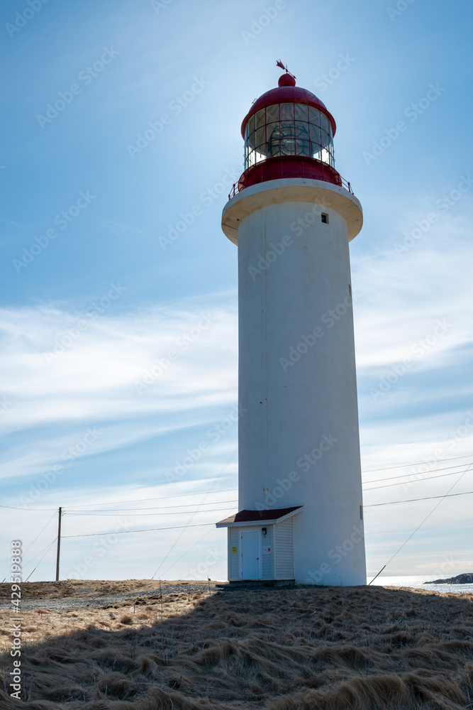 A vintage lighthouse tower with a round red metal roof.  In the center of the lighthouse is a vintage lamp made of multiple pieces of glass. On top of the white tower is a red metal wind arrow.