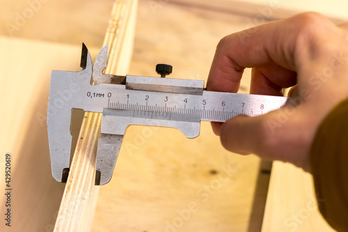 male hand holds an old mechanical vernier caliper, measures the thickness of plywood photo