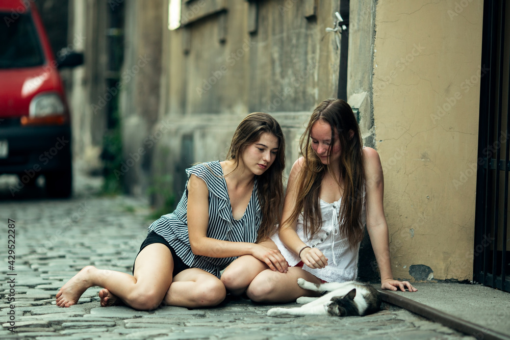 Two teenage girls sitting on the pavement with a cat. Two teenage girls sitting on the pavement with a cat.