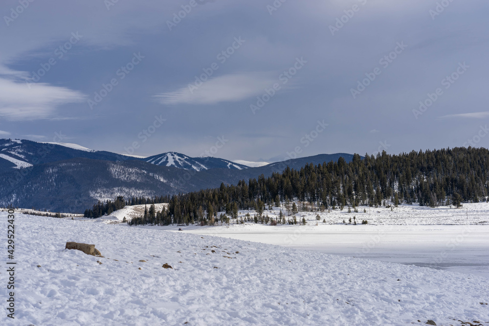 View of ski slopes on mountains behind frozen LakeDillon Colorado on partly cloudy winter day