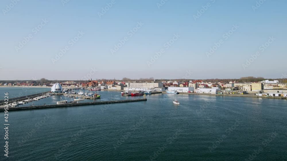 Hel Peninsula before the season, a white sailboat enters the harbor on the calm water of the Puck Bay, slow motion aerial, Poland Hel Peninsula before the season, a white sailboat enters the harbor on the calm water of the Puck Bay, slow motion aerial, Poland
