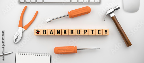 wooden cubes with the message BANKRUPTCY surrounded by handiman tools and office equipment on white background photo