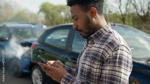 Young Male Driver Contacting Car Insurance Company By Text On Mobile Phone After Traffic Accident