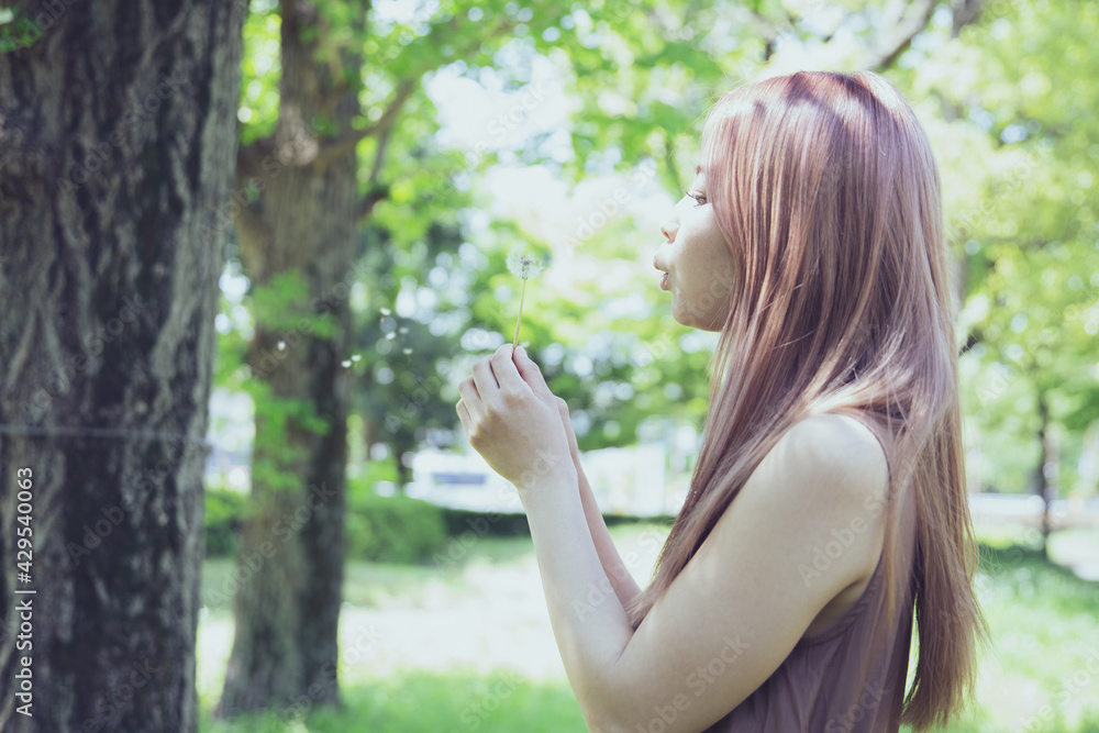 たんぽぽの綿毛を吹く美しい女性のポートレート