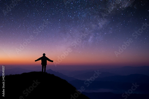 Silhouette of young traveler and backpacker looking beautiful view of night sky and star and milky way alone on top of the mountain. He enjoyed traveling and was successful when he reached the summit.