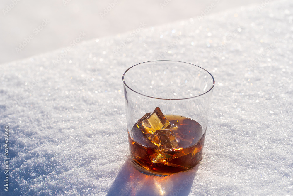 Glass of whiskey with ice on a bed of snow and white background, close up