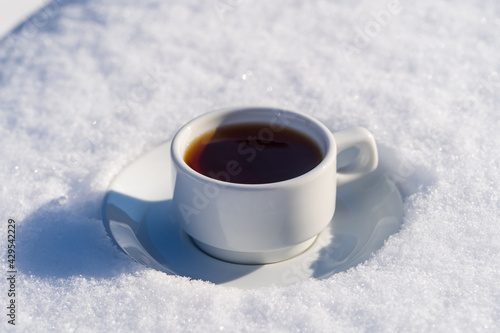 White cup of hot coffee on a bed of snow and white background, close up