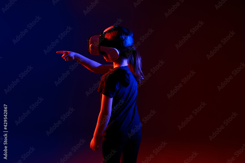 Fascinated child in dark shirt wearing virtual reality glasses over colour background