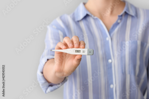 Woman with electronic thermometer on grey background  closeup